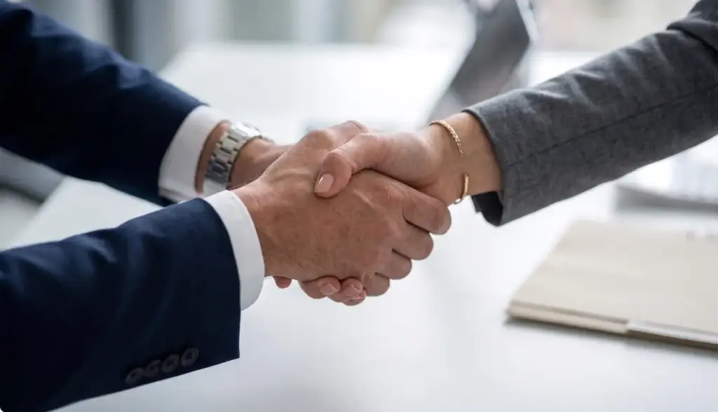 Primer plano de un apretón de manos profesional entre abogado y cliente, simbolizando un acuerdo legal formal, confianza y compromiso en un entorno de oficina moderno.